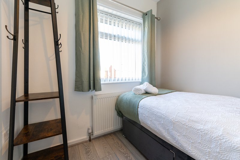 Bright bedroom with single bed, wooden ladder, window with green curtains and radiator