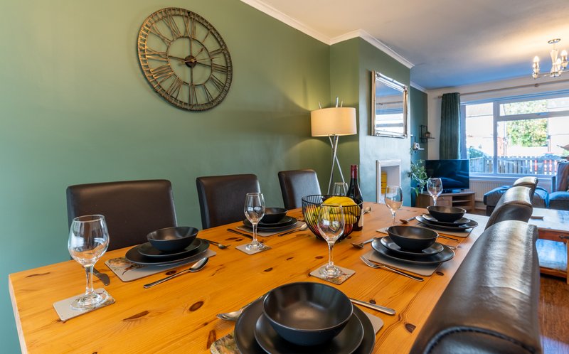 Dining room with wooden table, place settings, clock on green wall and views to lounge