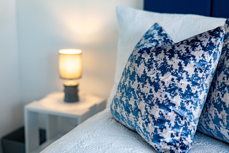 Bedroom with decorative blue patterned pillows, bedside lamp and modern nightstand