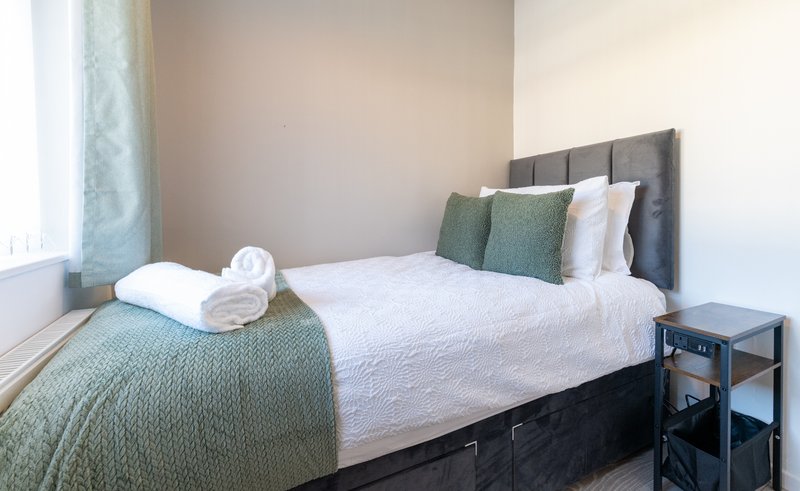 Modern bedroom with double bed, grey headboard, green throw and white pillows