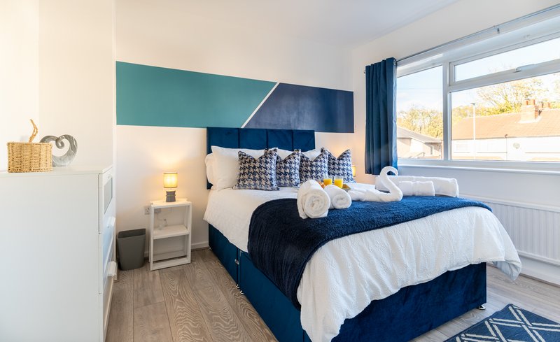 Modern bedroom with double bed, blue headboard, white bedding, and large window with countryside view