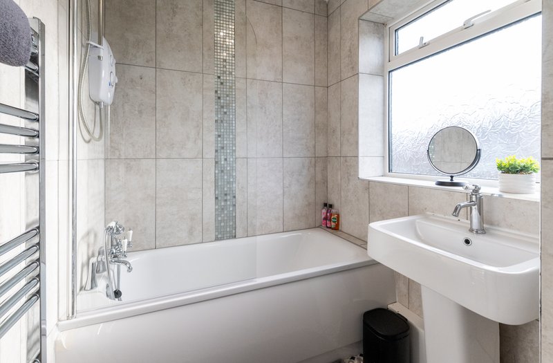 Modern bathroom with white bathtub, pedestal sink, tiled walls and window