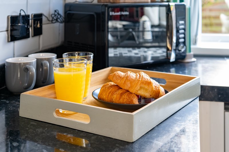 Modern kitchen with breakfast tray holding croissants, orange juice and mugs, black appliances and window view
