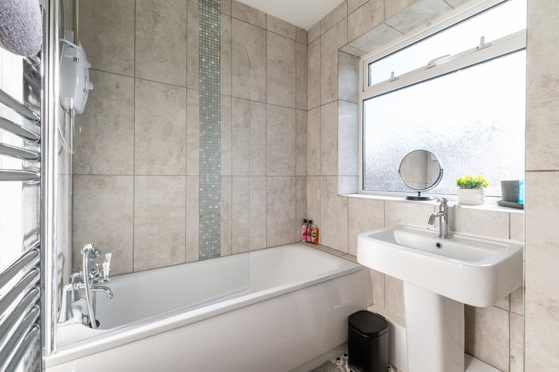Clean modern bathroom with bathtub, pedestal sink, heated towel rail and window