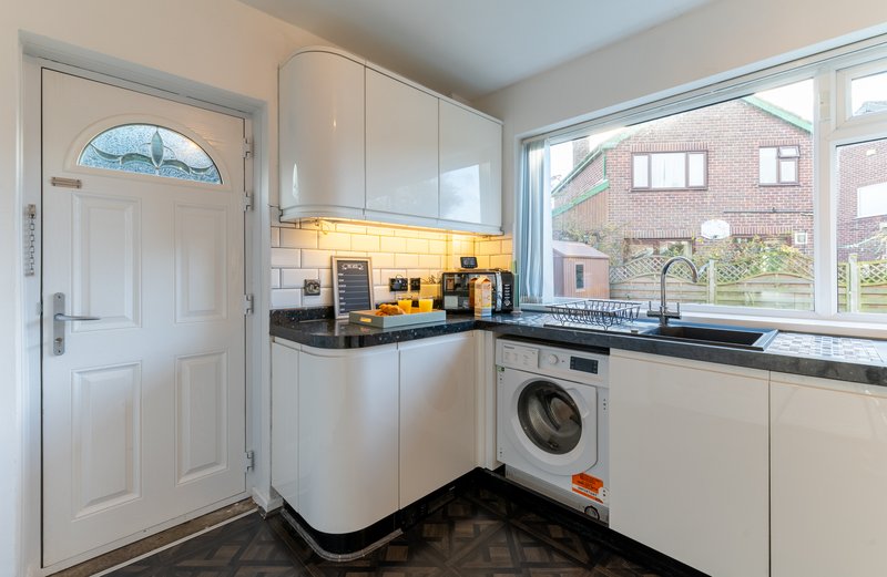 Modern kitchen with white cabinetry, black countertop, yellow backsplash, washing machine and window view