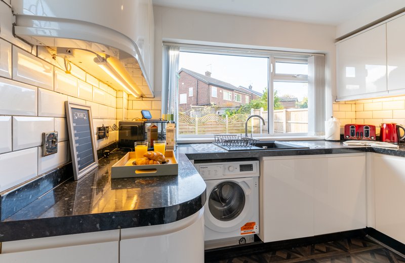 Modern kitchen with curved black countertop, white cabinetry, integrated appliances and window view