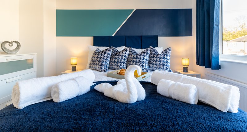 Modern bedroom with twin beds, blue headboard, patterned pillows and rolled white towels