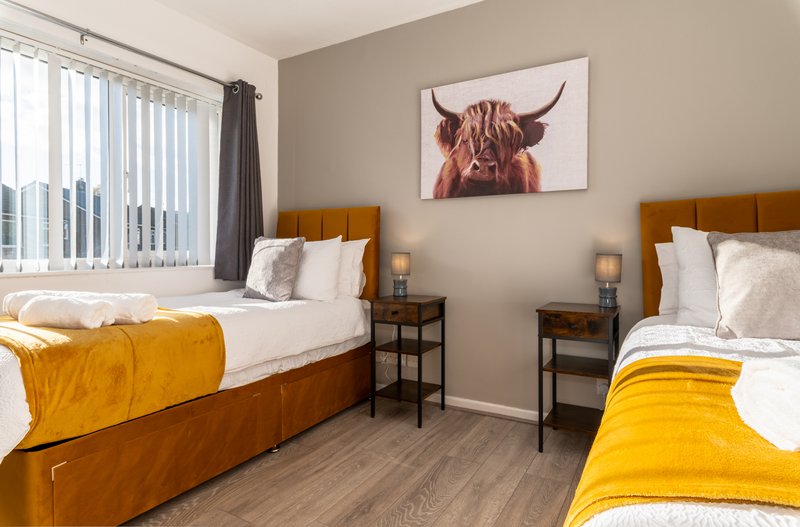 Twin bedroom with yellow blankets, wooden headboards, and Highland cattle wall art