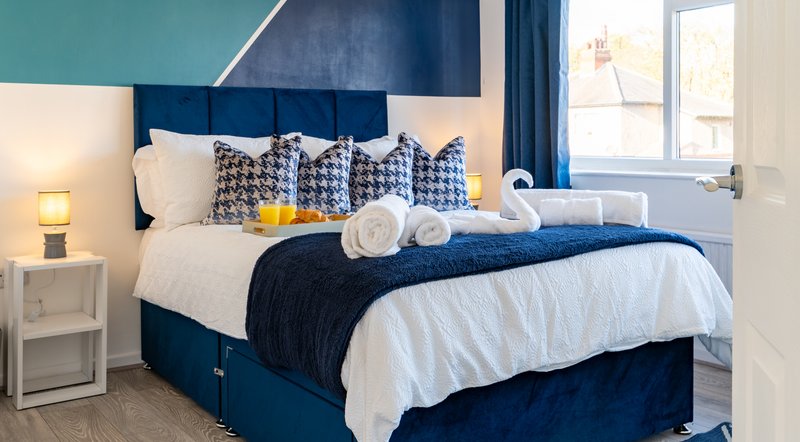 Modern bedroom with blue upholstered bed, white bedding, rolled towels, and patterned pillows