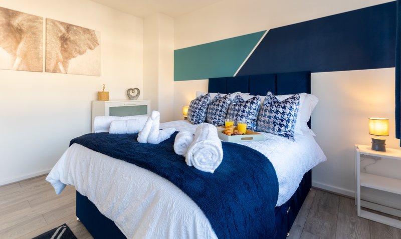 Modern bedroom with double bed, navy headboard, rolled towels and yellow accents