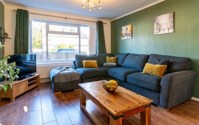 Modern living room with blue corner sofa, wooden coffee table, green accent wall and bay window