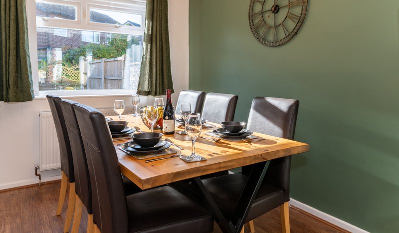 Dining room with wooden table, black chairs, place settings, and garden view from window