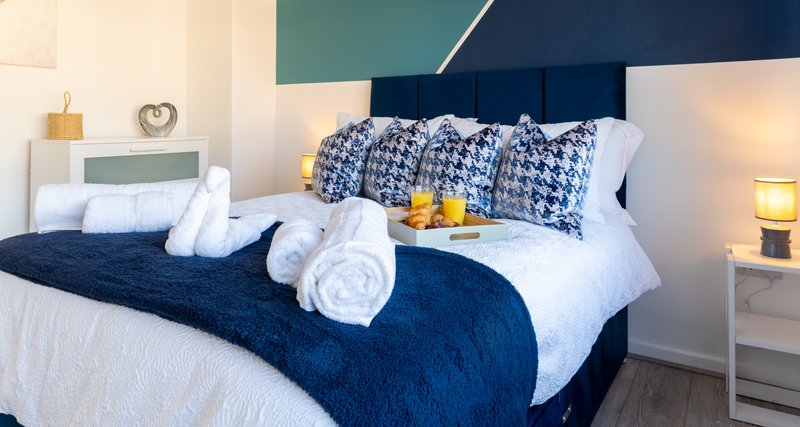 Modern bedroom with navy blue upholstered bed, white pillows, patterned cushions and rolled towels