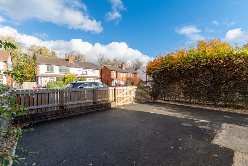 Driveway with wooden fencing, parked car, brick houses and hedges visible
