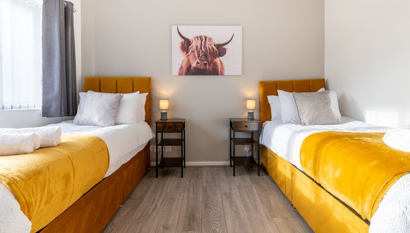 Twin bedroom with two single beds, yellow bedding, wooden headboards and bedside tables
