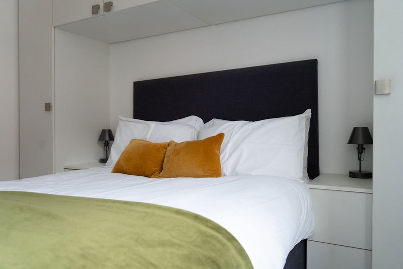 Modern bedroom with black headboard, white bedding, gold cushions and green throw blanket