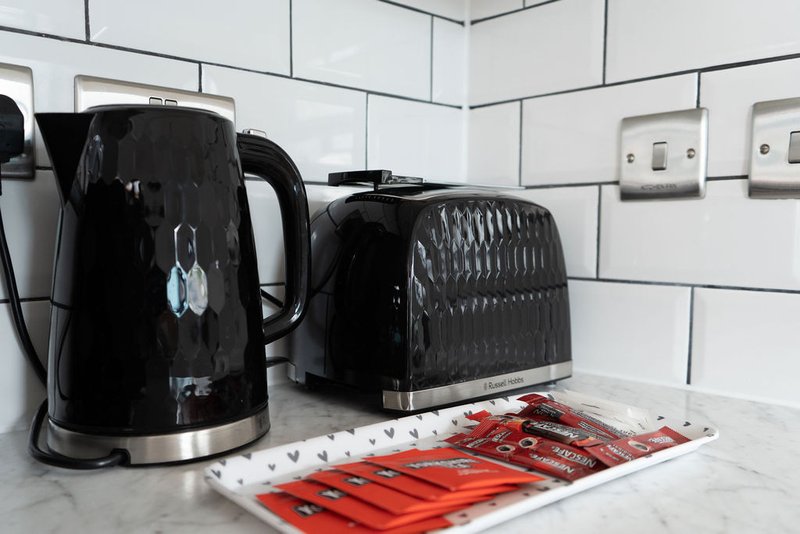 Kitchen countertop with black kettle, black toaster, and red kitchen tools on white subway tile backsplash