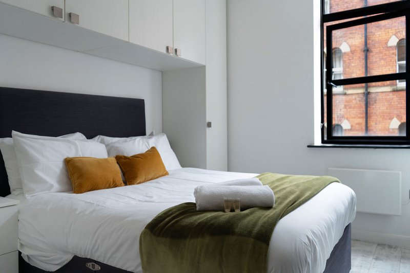 Modern bedroom with double bed, black headboard, white bedding, mustard cushions and olive throw