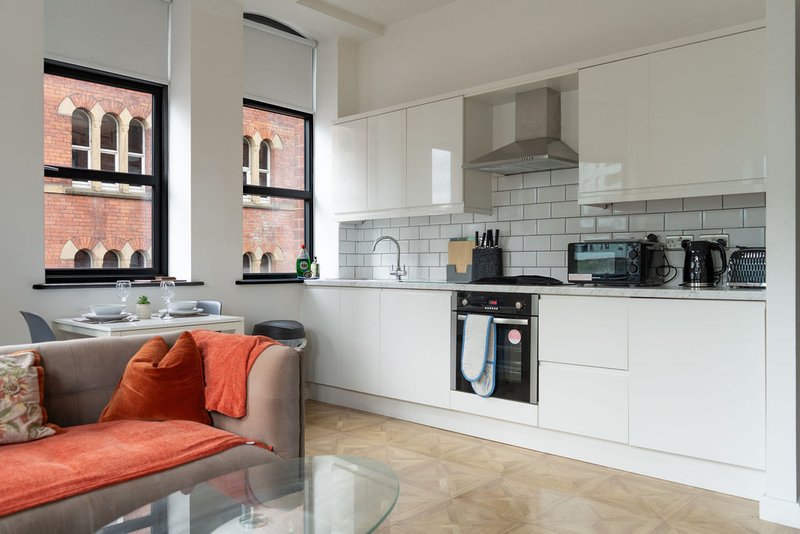 Open-plan kitchen and living area with white cabinetry, brick building view through windows, and orange accent seating