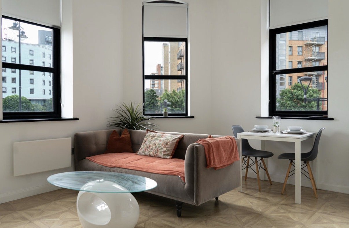 Bright studio apartment with grey sofa, round coffee table, desk and city views from windows