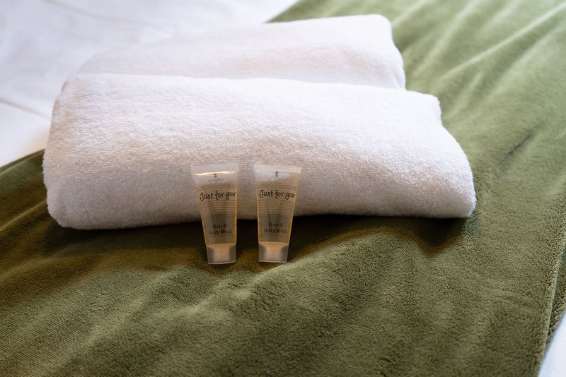 Folded white towels with small toiletry bottles on green bedding