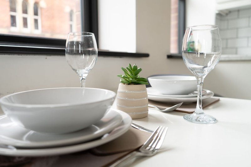 Dining table set with white plates, glasses, cutlery and small potted plant