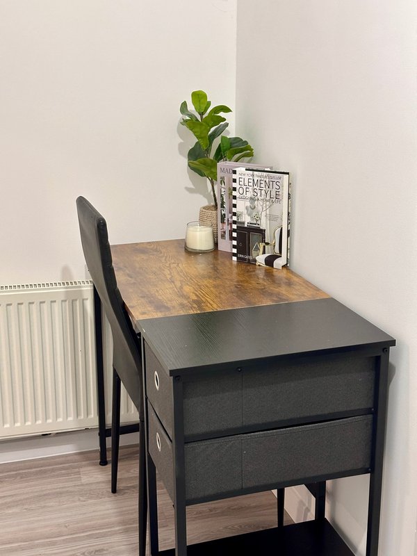 Small black desk with wooden top, chair, potted plant, and desk accessories in corner room