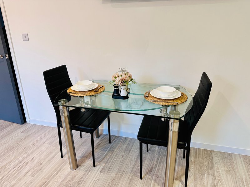Glass dining table with two black chairs, place settings, and floral centerpiece