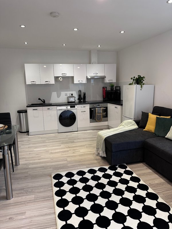 Open-plan kitchen and living area with white cabinetry, black appliances, and black and white checkered rug