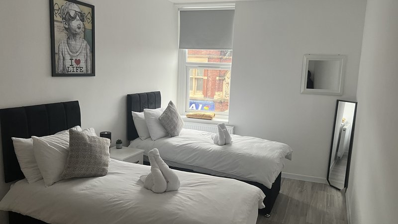 Modern bedroom with two single beds, white bedding, grey cushions and neutral decor
