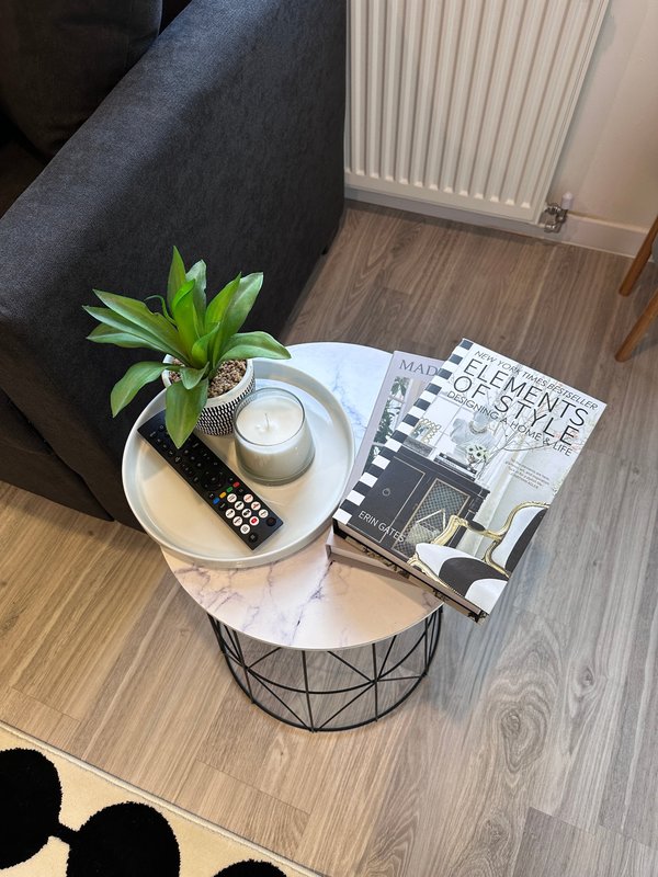 Small side table with potted plant, candle, remote control and magazine next to grey sofa