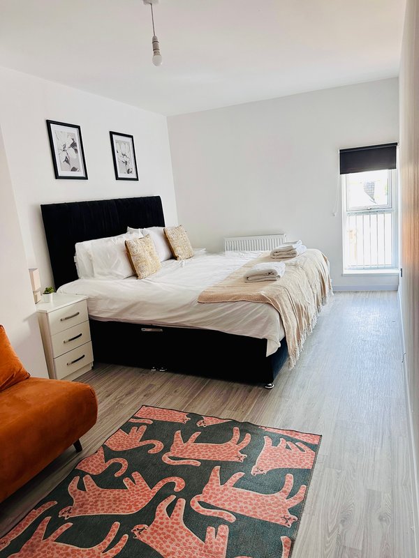 Bright bedroom with black bed frame, white bedding, wooden flooring and patterned rug