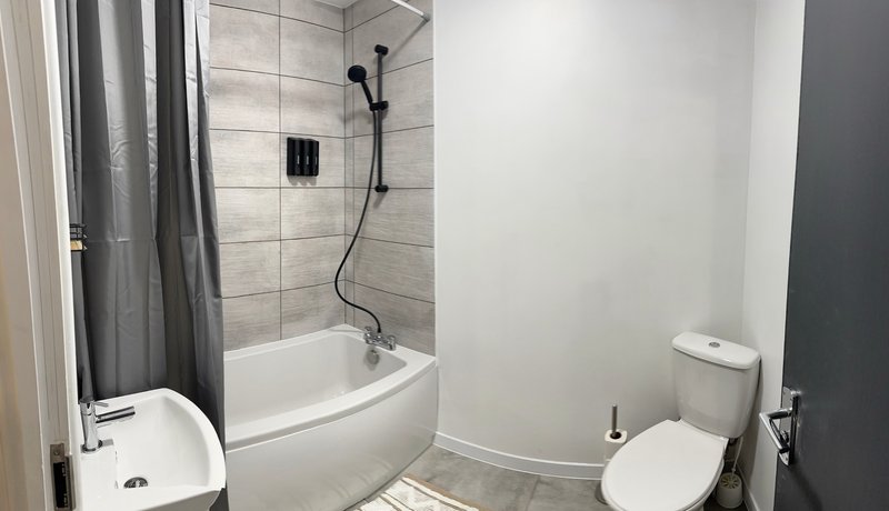 Bathroom with toilet, bathtub, shower enclosure, and grey tile walls