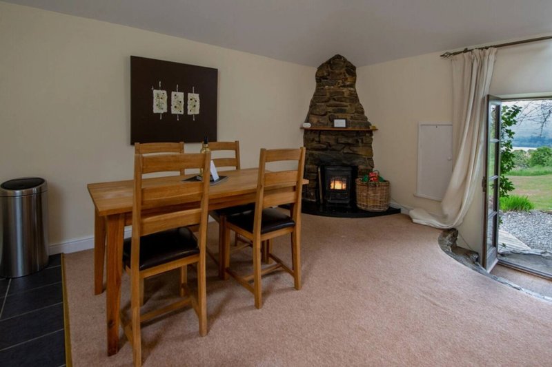 Open-plan living area with wooden dining table, stone fireplace with wood burner, and patio doors to garden