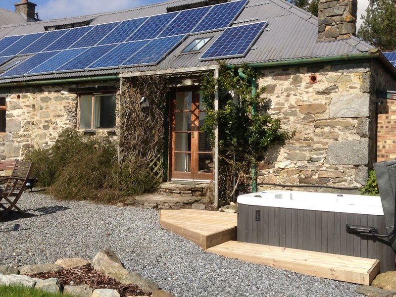 Stone cottage exterior with solar panels, wooden deck, gravel courtyard and hot tub