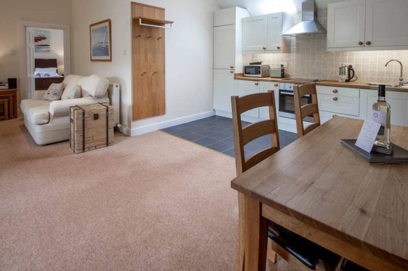 Open-plan living and kitchen area with cream armchair, wooden dining table, and white cabinetry