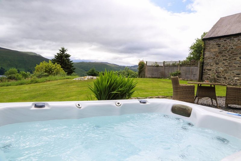 Hot tub with mountain views, stone building, and manicured garden with trees
