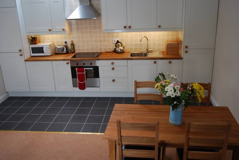 Modern kitchen with white cabinetry, wooden countertop, dining table and fresh flowers in vase