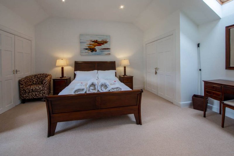 Spacious bedroom with wooden bed, white bedding, two bedside lamps, and patterned armchair