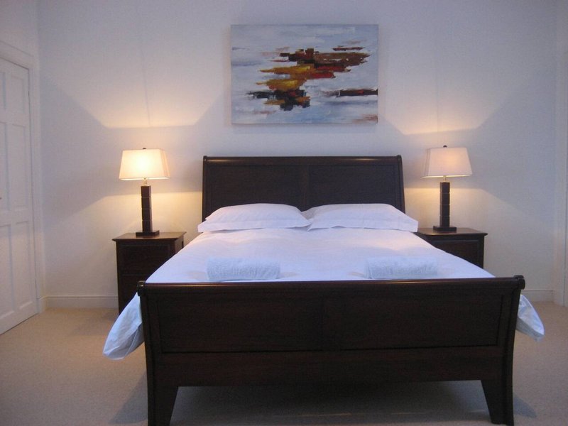 Modern bedroom with black bed frame, white bedding, two bedside lamps and abstract wall art