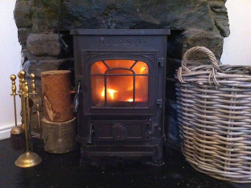 Wood-burning stove with fireplace tools, wicker basket, and rustic stone surround