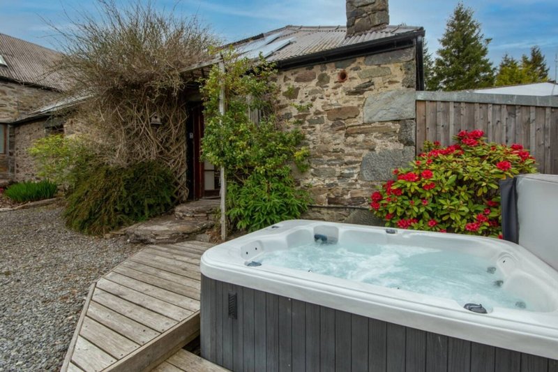 Outdoor hot tub on wooden deck with stone cottage, garden plants and countryside views
