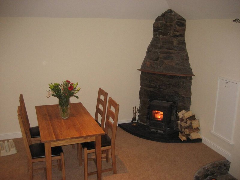 Dining area with wooden table, chairs, flowers, and decorative fireplace with stove