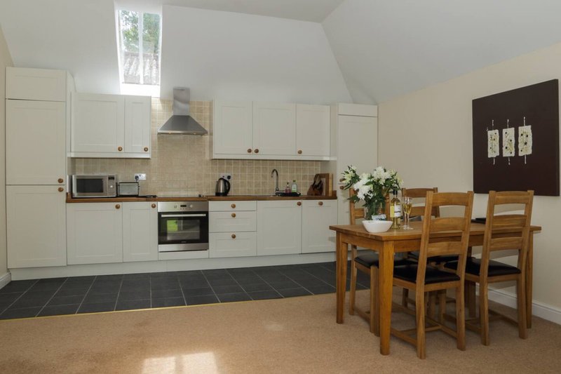 Open-plan kitchen and dining area with white cabinetry, wooden table and chairs, dark tile floor