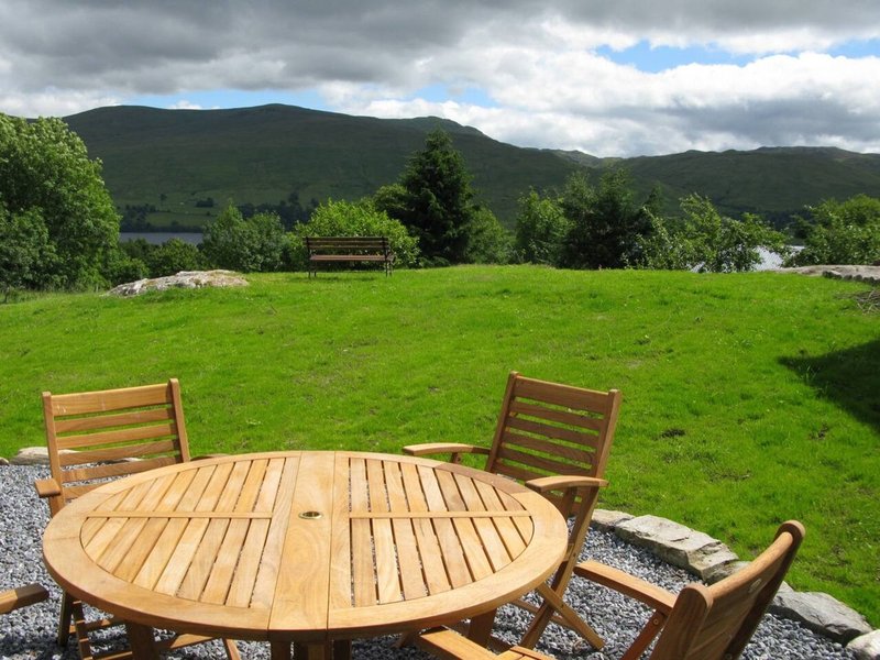 Wooden garden table and chairs on patio overlooking green lawn and mountains