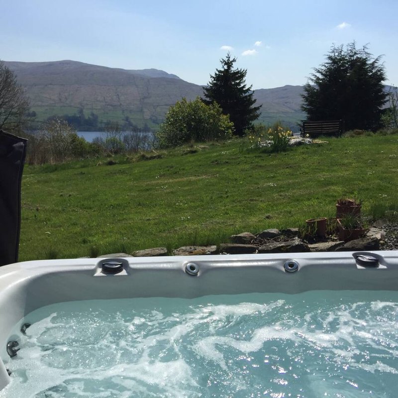 Hot tub with mountain and lake views, green garden with trees in background