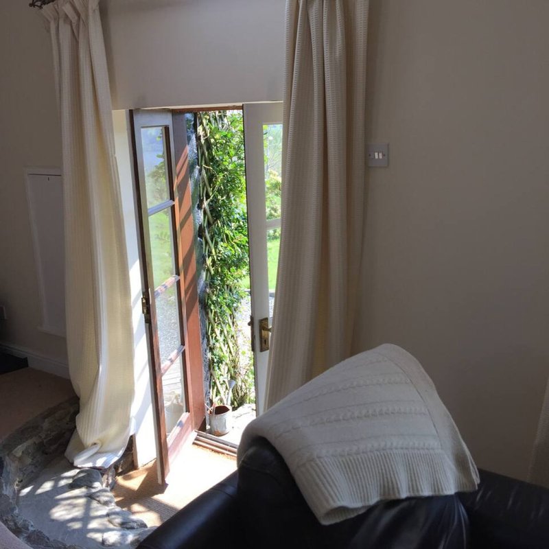 Bedroom with glass door opening to ivy-covered exterior, cream curtains and bed