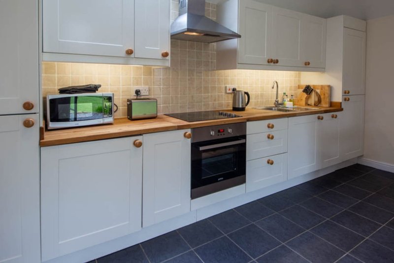 Modern kitchen with white cabinetry, wooden worktops, black oven and tiled backsplash