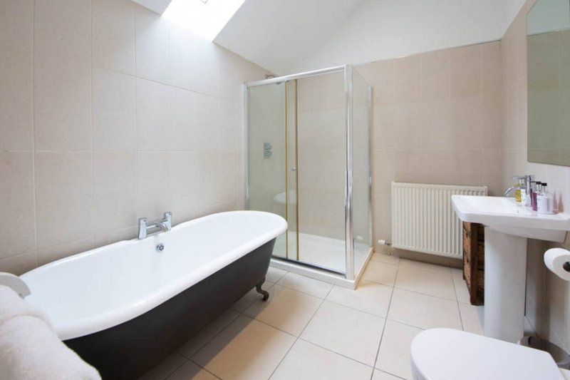 Modern bathroom with black freestanding bathtub, walk-in shower enclosure, pedestal sink and toilet
