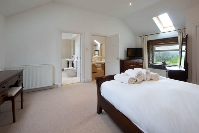 Bright bedroom with double bed, wooden frame, white bedding, en-suite bathroom and countryside views